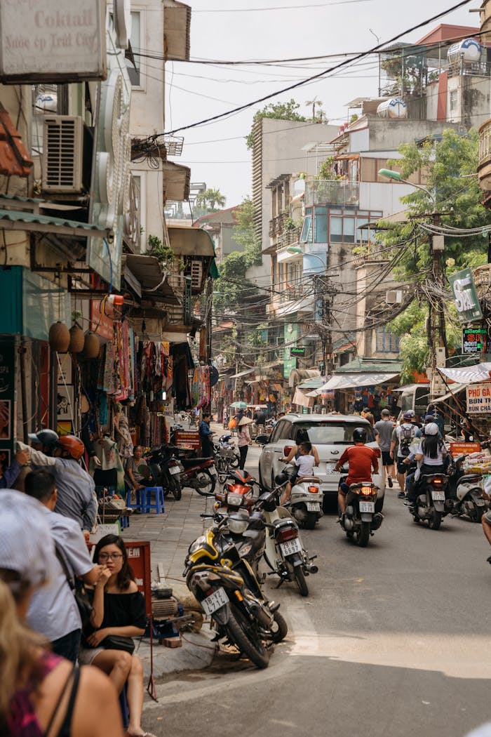 gallery-03 Vibrant street life in Dong Da, Hanoi, with motorbikes, shops, and pedestrians on a sunny day.